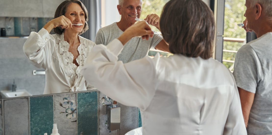 older people brushing their teeth in front of a mirror - Look After Your Teeth In Older Age
