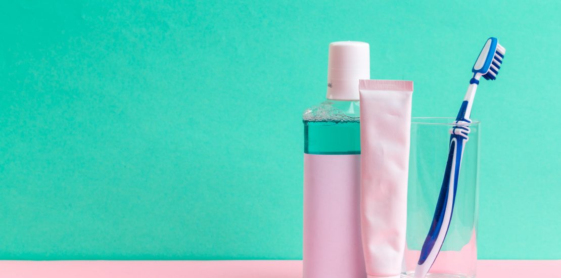 toothbrush, toothpaste and mouthwash standing on a green background