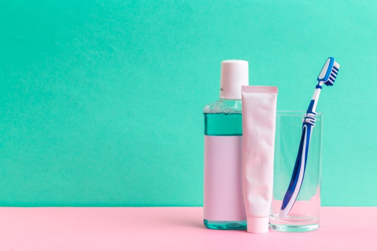 toothbrush, toothpaste and mouthwash standing on a green background