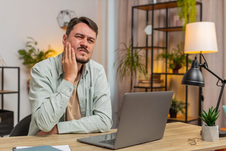 caucasian young man freelancer sitting home office table feeling toothache touching mouth home 1 1